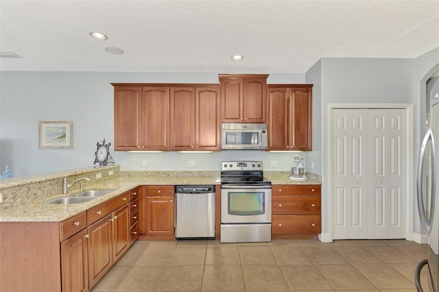 kitchen with light stone counters, light tile patterned flooring, appliances with stainless steel finishes, and sink