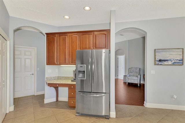 kitchen with light hardwood / wood-style floors, stainless steel fridge, a textured ceiling, and light stone counters