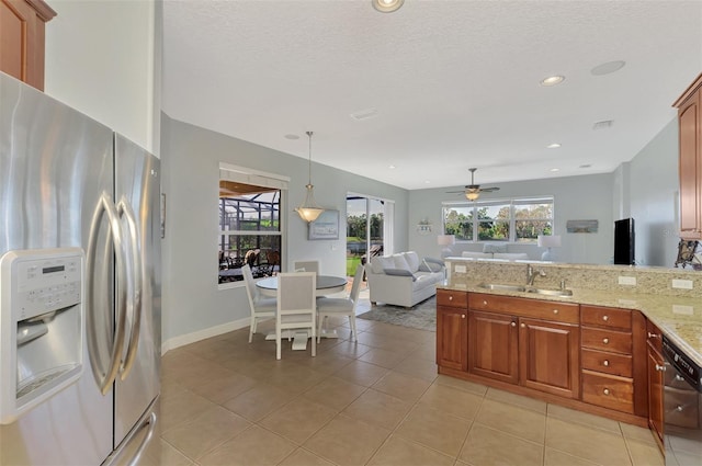 kitchen with sink, stainless steel fridge, pendant lighting, light stone counters, and ceiling fan