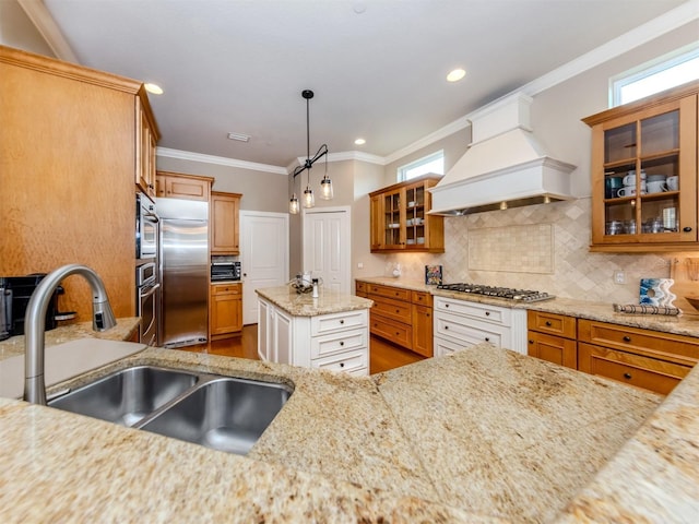 kitchen with white cabinets, hanging light fixtures, appliances with stainless steel finishes, light stone counters, and custom range hood