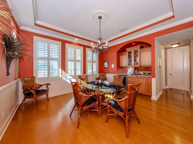 dining room with a raised ceiling, light wood-type flooring, an inviting chandelier, and ornamental molding