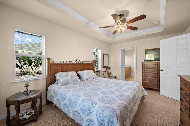 bedroom featuring light carpet, ensuite bathroom, a tray ceiling, and ceiling fan