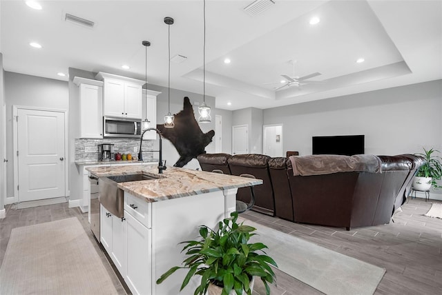 kitchen featuring white cabinetry, light stone counters, a tray ceiling, and an island with sink