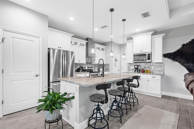 kitchen with an island with sink, pendant lighting, white cabinetry, appliances with stainless steel finishes, and light stone counters