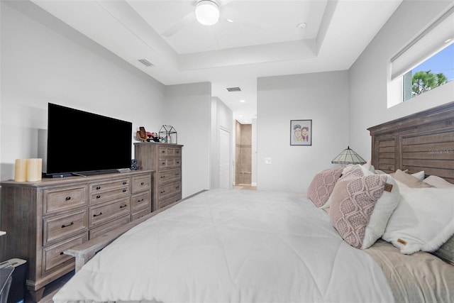 bedroom with ceiling fan, a raised ceiling, and ensuite bathroom