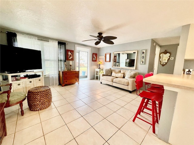 living room with ceiling fan, light tile patterned floors, and a textured ceiling