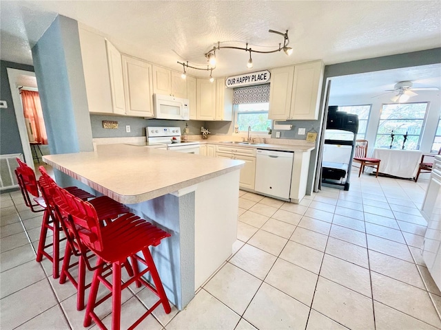 kitchen with a textured ceiling, a kitchen bar, white appliances, and kitchen peninsula