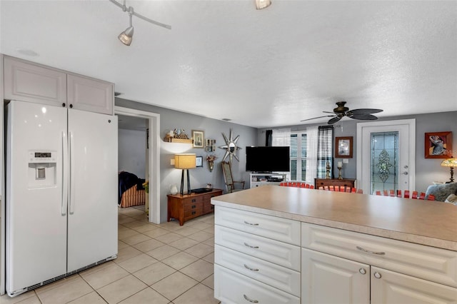 kitchen with white refrigerator with ice dispenser, white cabinets, ceiling fan, light tile patterned floors, and a textured ceiling