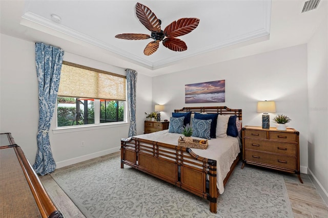 bedroom with crown molding, light hardwood / wood-style flooring, a tray ceiling, and ceiling fan