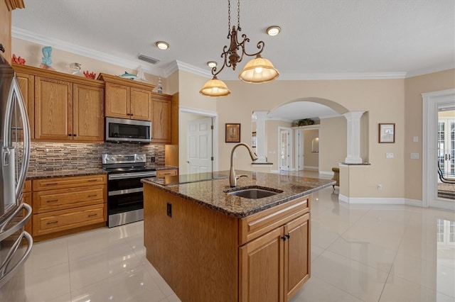 kitchen featuring appliances with stainless steel finishes, sink, decorative columns, pendant lighting, and a center island with sink