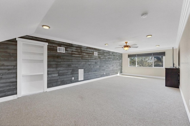 unfurnished living room with crown molding, wooden walls, light colored carpet, and built in shelves