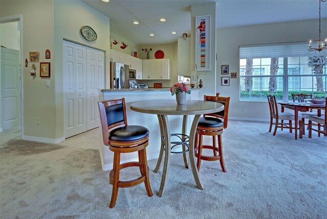 kitchen with light carpet, hanging light fixtures, appliances with stainless steel finishes, white cabinetry, and a chandelier