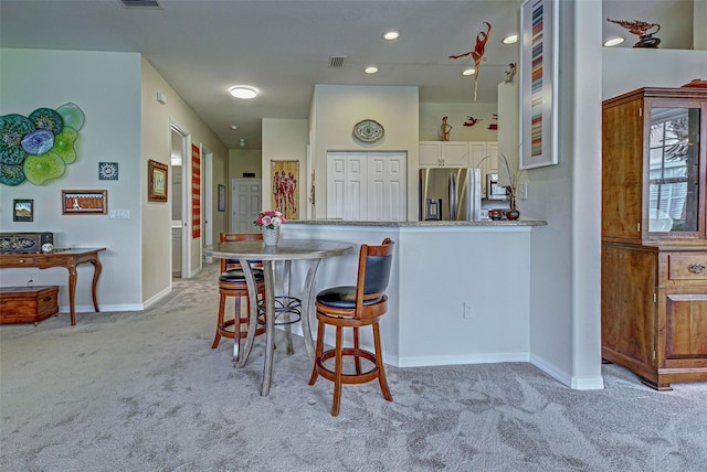 kitchen with a breakfast bar area, stainless steel fridge, light stone countertops, and light carpet