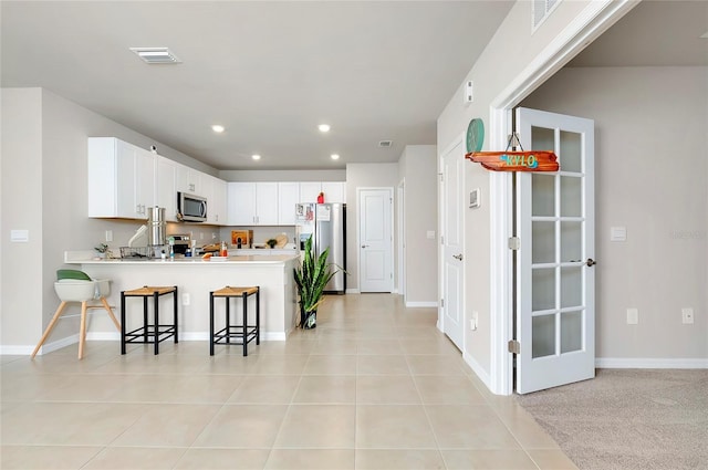 kitchen with appliances with stainless steel finishes, a kitchen bar, kitchen peninsula, white cabinets, and light tile patterned floors