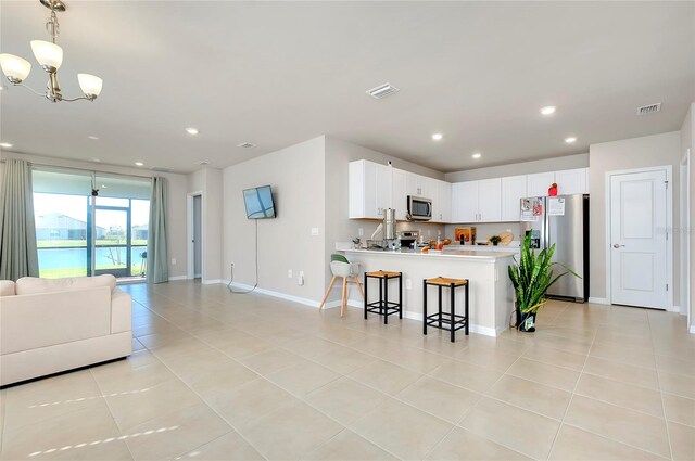 kitchen featuring kitchen peninsula, white cabinets, light tile patterned floors, appliances with stainless steel finishes, and a kitchen breakfast bar