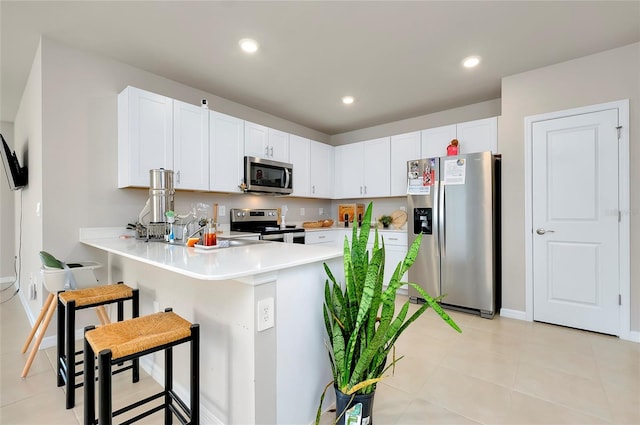 kitchen with kitchen peninsula, white cabinets, light tile patterned floors, appliances with stainless steel finishes, and a breakfast bar