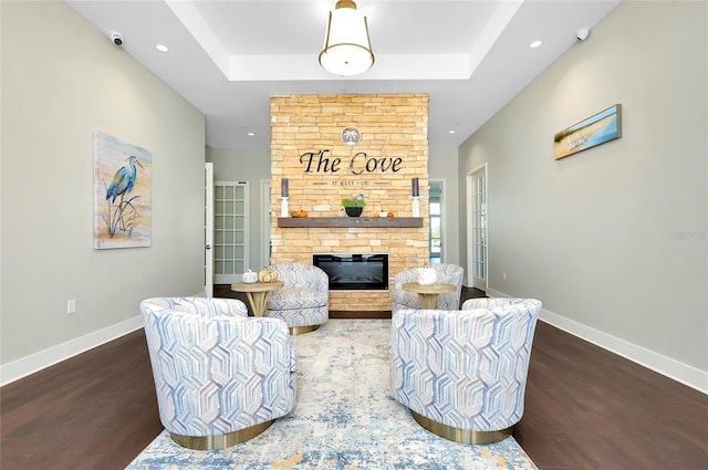 living room with a stone fireplace, a tray ceiling, and dark hardwood / wood-style flooring