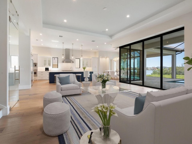 living room with a tray ceiling, sink, and light hardwood / wood-style floors