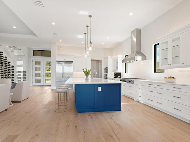 kitchen featuring appliances with stainless steel finishes, light wood-type flooring, exhaust hood, white cabinetry, and an island with sink