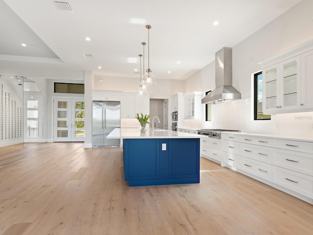 kitchen with island exhaust hood, appliances with stainless steel finishes, pendant lighting, light hardwood / wood-style floors, and white cabinetry