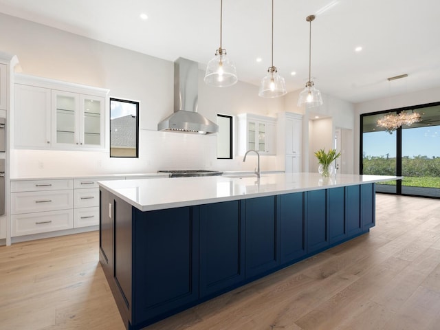 kitchen with white cabinets, pendant lighting, light hardwood / wood-style flooring, and wall chimney exhaust hood