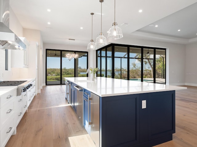 kitchen featuring blue cabinets, sink, light hardwood / wood-style flooring, range hood, and white cabinetry