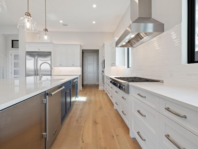 kitchen with white cabinetry, extractor fan, decorative light fixtures, appliances with stainless steel finishes, and light wood-type flooring