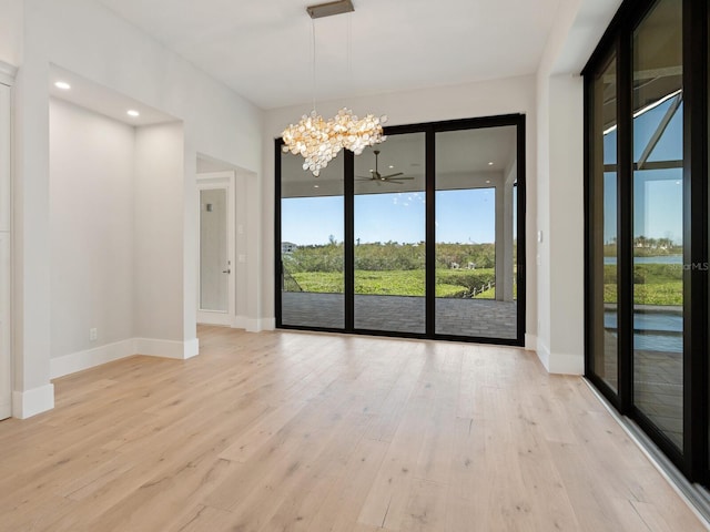 unfurnished dining area with ceiling fan with notable chandelier, light wood-type flooring, and a wealth of natural light