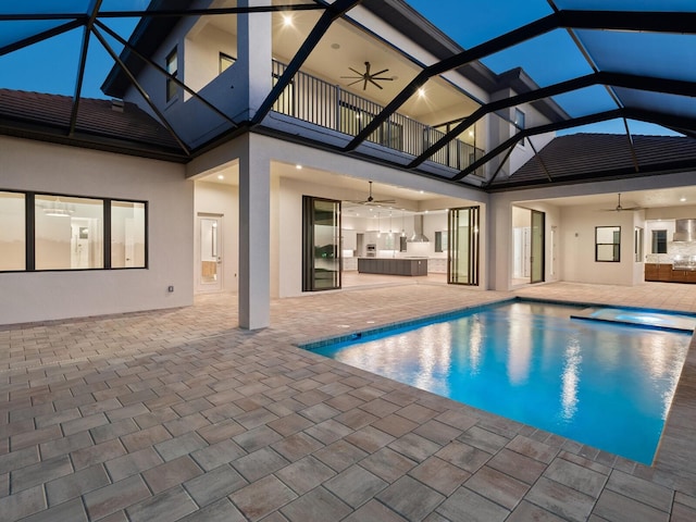 view of pool featuring a patio, glass enclosure, ceiling fan, and exterior kitchen