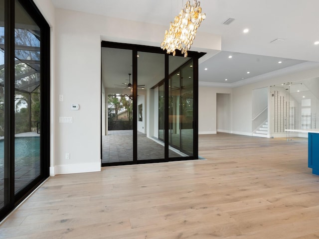 empty room featuring ceiling fan with notable chandelier, light hardwood / wood-style flooring, and a healthy amount of sunlight