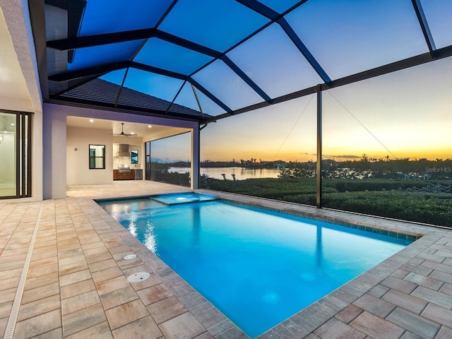 pool at dusk featuring a lanai, ceiling fan, a water view, and a patio