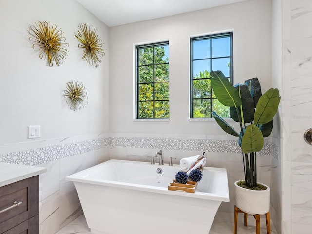 1109 Bayshore Rd, Nokomis, FL 34275 - bathroom with marble look tile flooring, a freestanding tub, vanity, tile walls, and a wainscoted wall