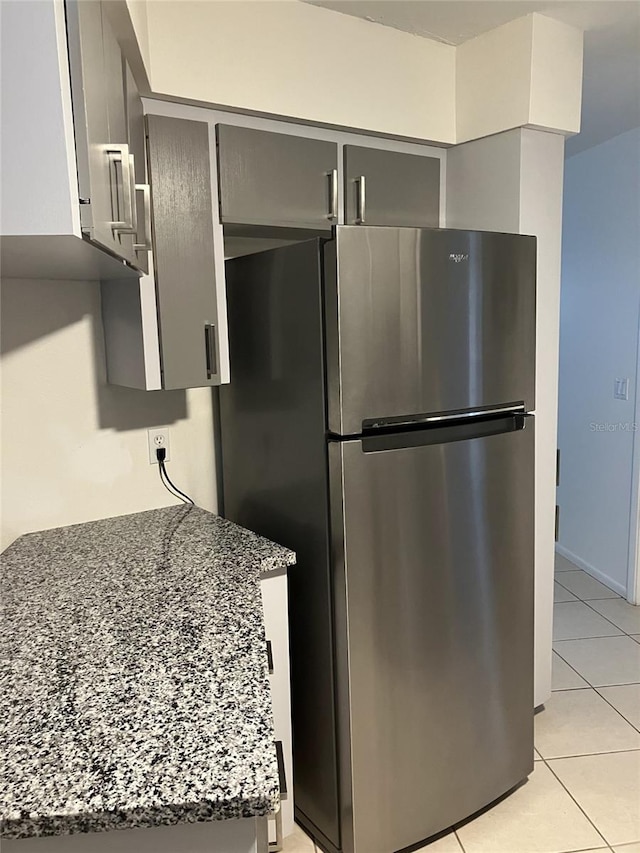 kitchen featuring light tile patterned floors, dark stone counters, stainless steel refrigerator, and gray cabinets