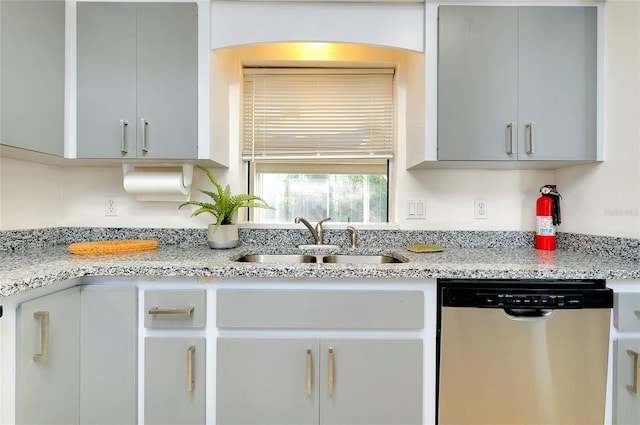 kitchen with stainless steel dishwasher, sink, and light stone counters