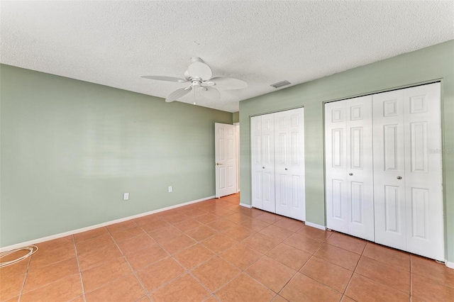 unfurnished bedroom with ceiling fan, a textured ceiling, light tile patterned floors, and two closets