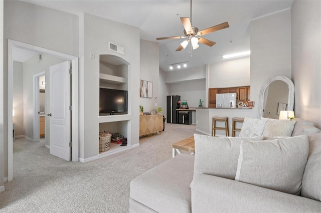 living room with light carpet, ceiling fan, a high ceiling, and built in shelves