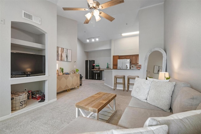 living room with ceiling fan, light carpet, a towering ceiling, and built in shelves