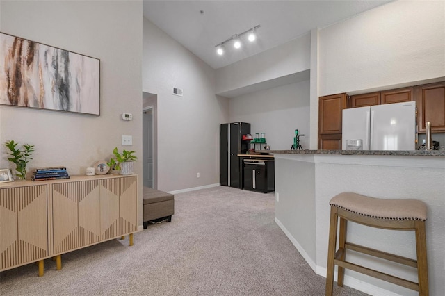 kitchen with a breakfast bar area, white fridge with ice dispenser, rail lighting, high vaulted ceiling, and light colored carpet