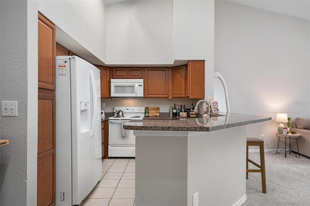 kitchen with kitchen peninsula, vaulted ceiling, light tile patterned flooring, a kitchen bar, and white appliances