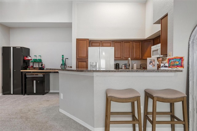 kitchen with light carpet, kitchen peninsula, a kitchen breakfast bar, and white appliances