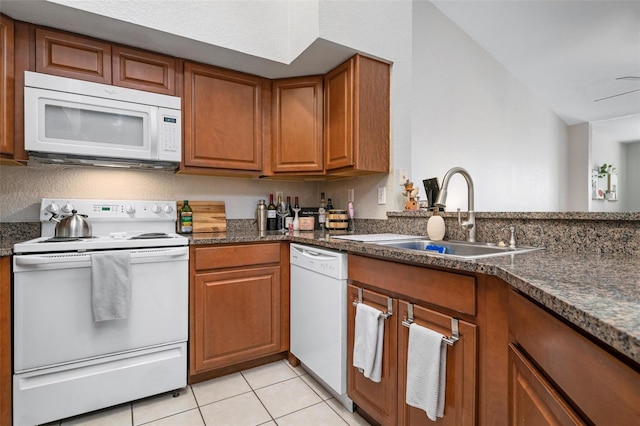 kitchen with sink, dark stone countertops, white appliances, and light tile patterned floors