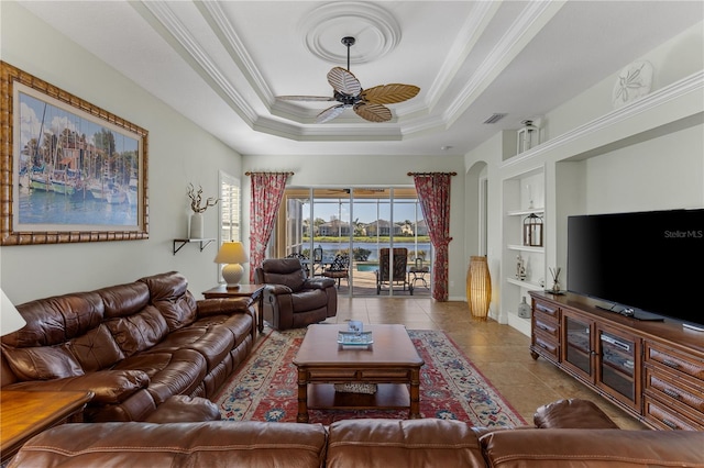 living room with built in features, crown molding, tile patterned flooring, a tray ceiling, and ceiling fan