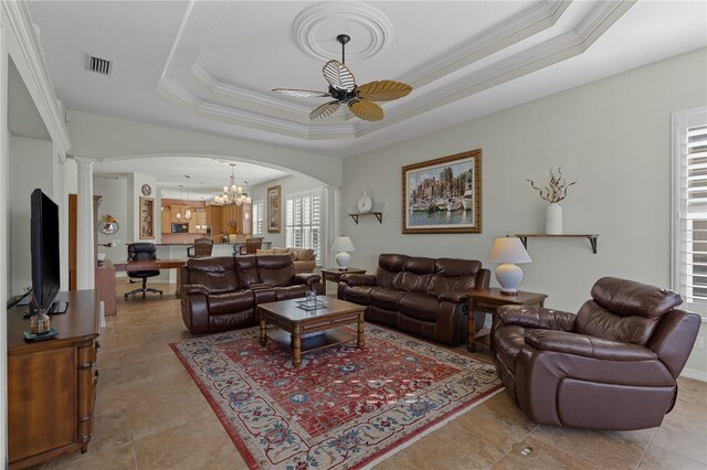 living room with ornate columns, ceiling fan with notable chandelier, ornamental molding, and a tray ceiling