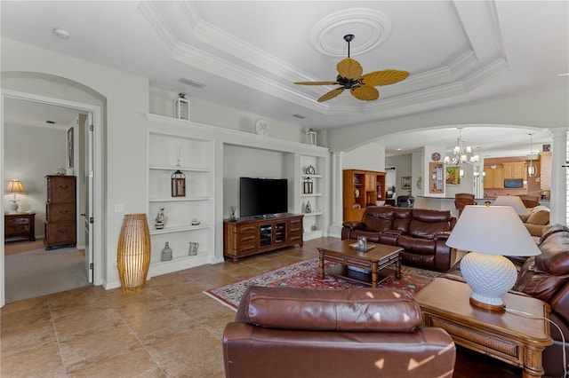 living room featuring arched walkways, a tray ceiling, ceiling fan with notable chandelier, and decorative columns