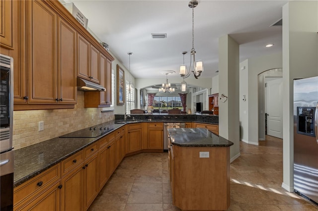 kitchen with a kitchen island, backsplash, stainless steel appliances, under cabinet range hood, and a notable chandelier