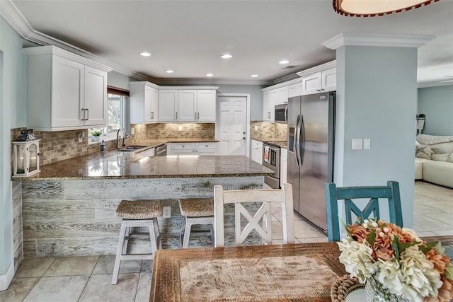 kitchen with crown molding, sink, appliances with stainless steel finishes, light tile patterned flooring, and a kitchen bar