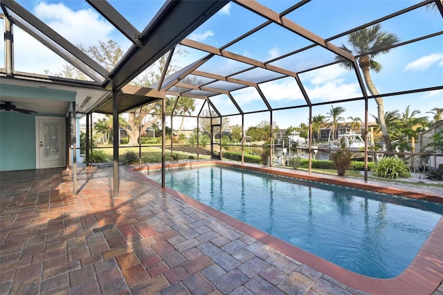 view of pool featuring a water view, glass enclosure, ceiling fan, and a patio area