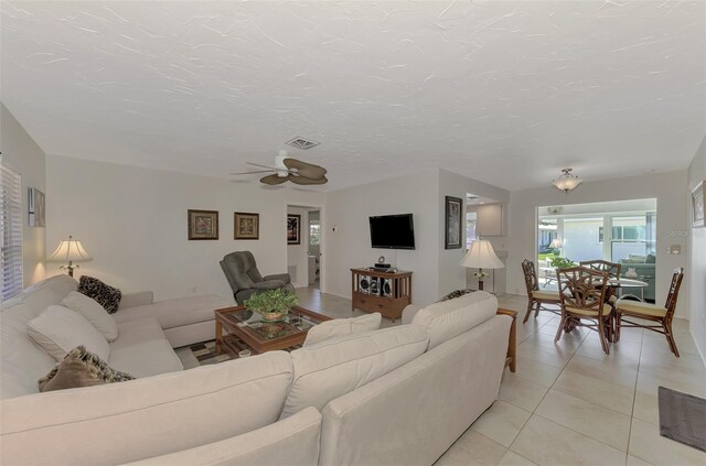 living room with a textured ceiling, light tile patterned floors, and ceiling fan