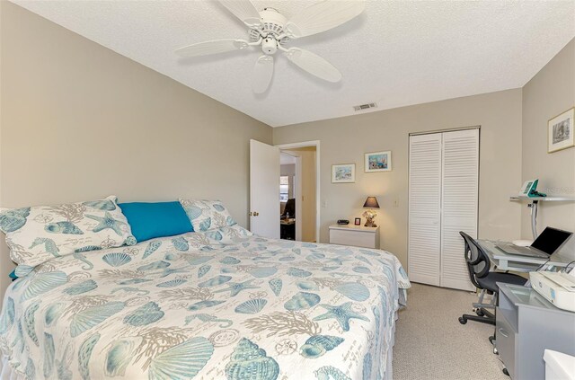 bedroom featuring a textured ceiling, light colored carpet, a closet, and ceiling fan