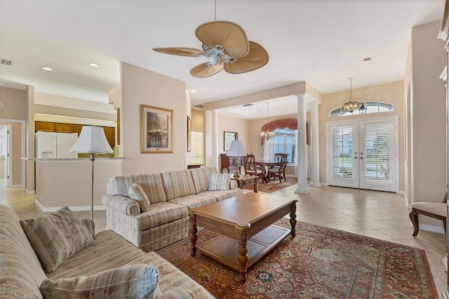 living room featuring ceiling fan with notable chandelier, french doors, light tile patterned floors, and decorative columns